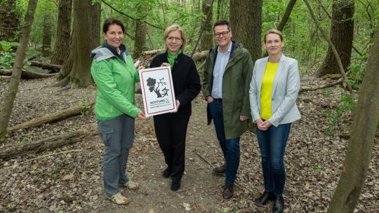 4 Personen stehen mit einer beschrifteten Tafel in einem Wald.