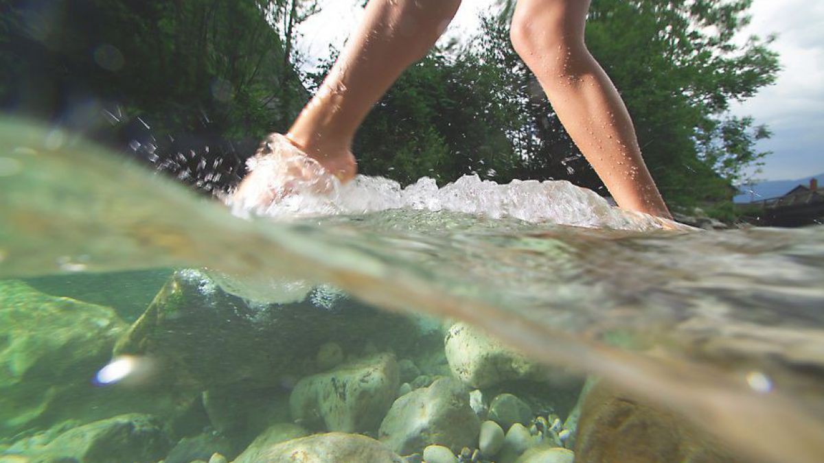 Füsse im Wasser, fotografiert an der Wasseroberfläche, so dass man die Füsse oberhalb und unterhalb des Wassers sieht