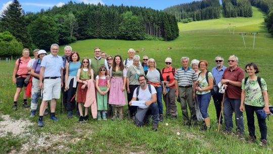 Gruppe von Menschen auf einer Wiese, dahinter ein Hang mit Wald