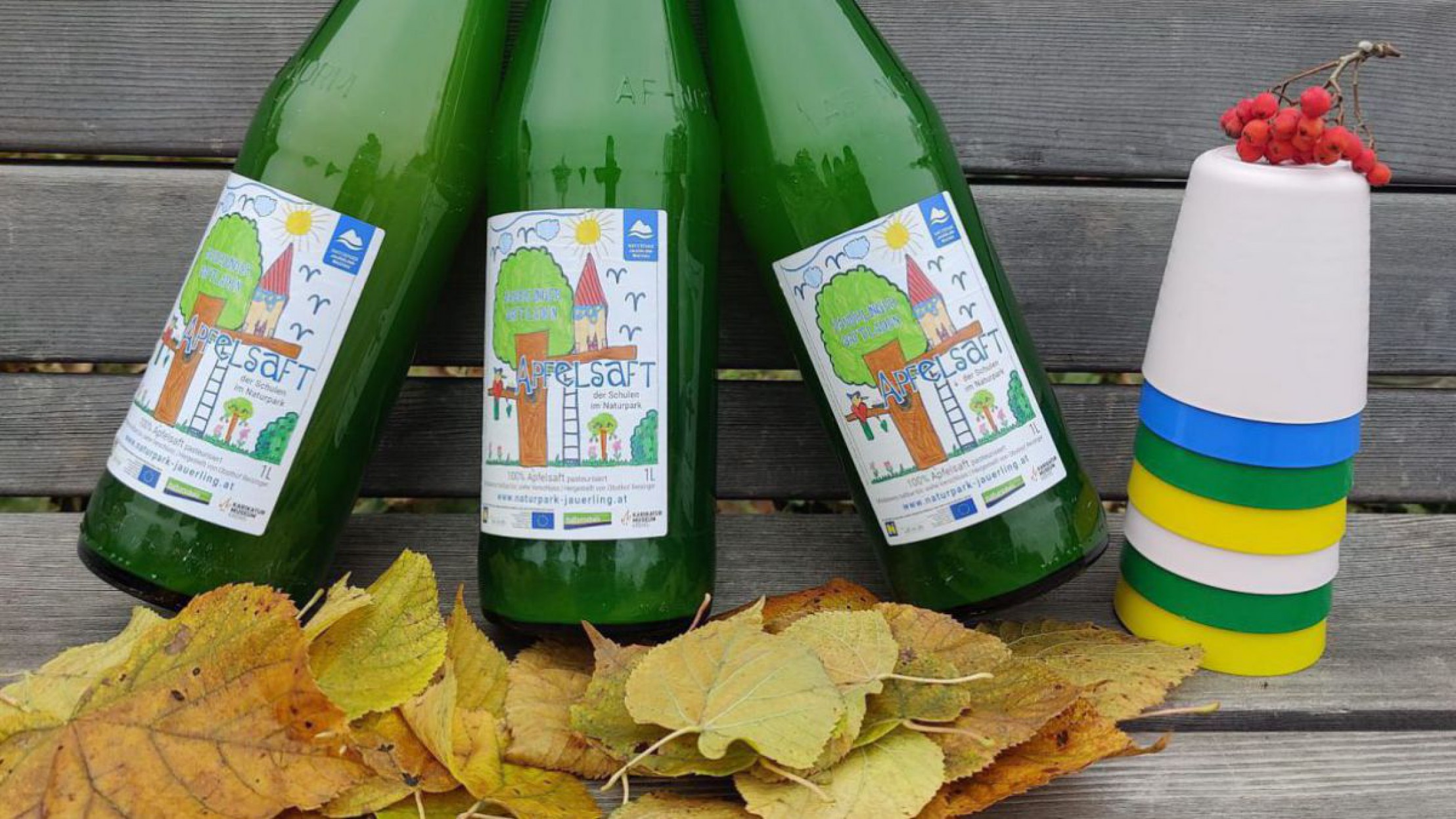 3 Flaschen mit Saft mit mehreren bunten Plastikbechern