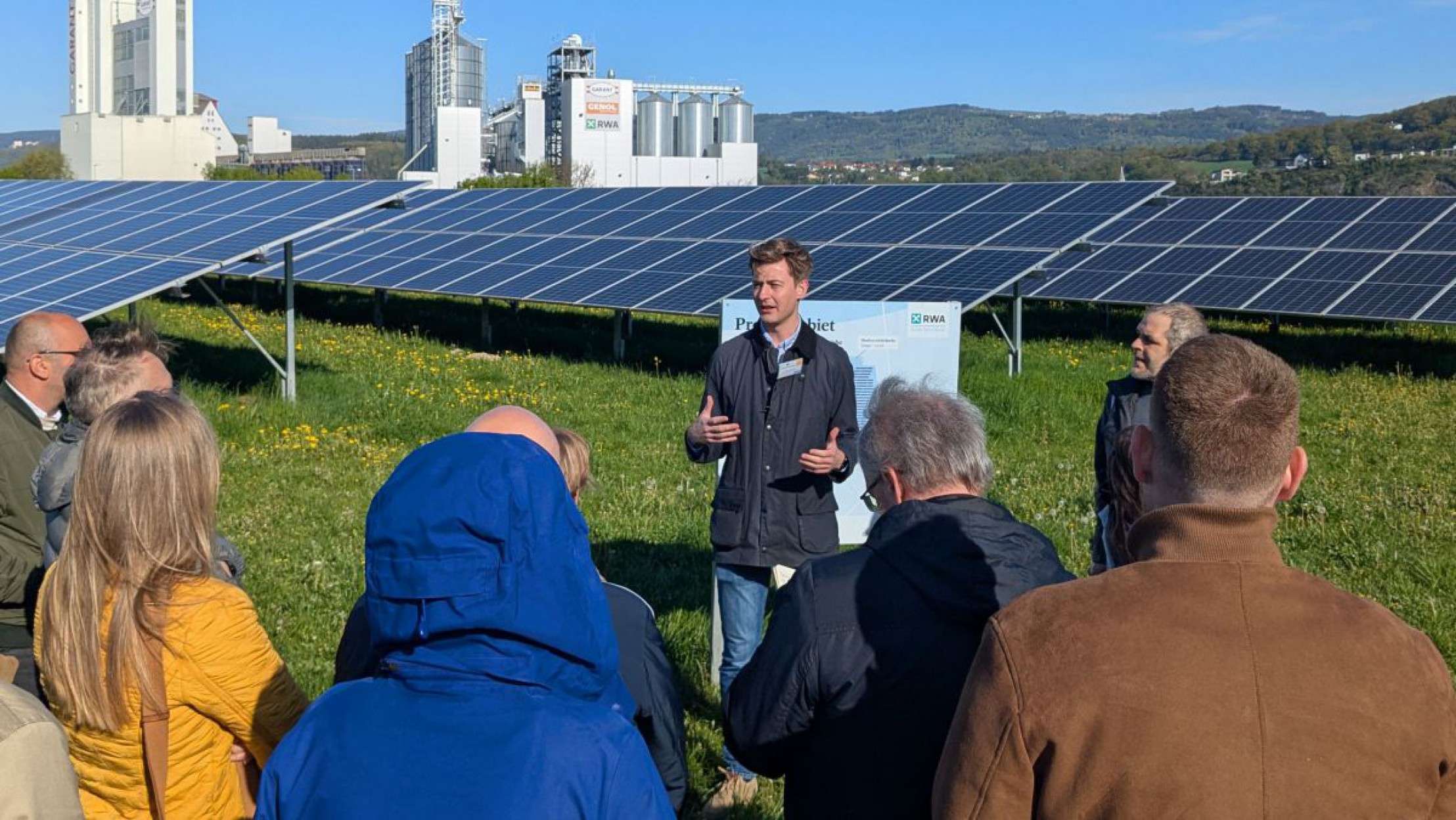 Eine Gruppe von fachkundigen Menschen unterh&auml;lt sich &uuml;ber eine Photovoltaikanlage, die auf einer landwirtschaftlich genutzten Fl&auml;che steht.