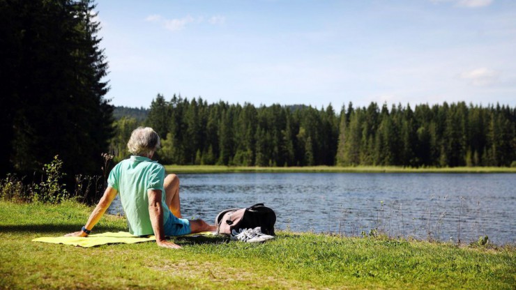 Mann sitzt am grasigen Ufer eines Sees und blickt in die Ferne.